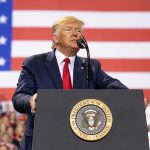 Trump Says Triumphal Arch Construction Just Two Months Away Man speaks at podium with U.S. flag background.