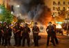 Riot Sparks Outside ICE Facility – Huge CLASH! Police officers in riot gear near burning car.