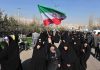 Group of women in black attire marching with an Iranian flag