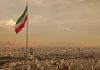 Iranian flag waving over a city skyline with mountains in the background