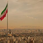 Coup Panic Grips Tehran Overnight – Regime Takeover! Iranian flag waving over a city skyline with mountains in the background