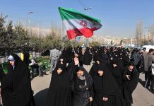 Talks After Bombs – Iran BEGGING For Truce! Group of women in black attire marching with an Iranian flag