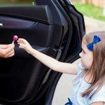 Child receiving lollipop from person in open car.