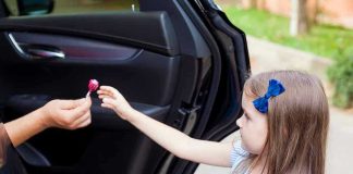 Child receiving lollipop from person in open car.
