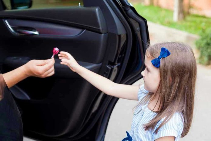 Child receiving lollipop from person in open car.