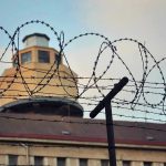 Trump Revives INFAMOUS Prison – It’s Back! Barbed wire in front of a prison tower.