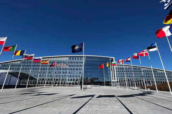 2284120437-1 Flags outside NATO headquarters building under clear blue sky.