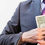 Person in suit putting dollars in jacket pocket.