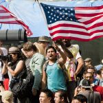 A diverse crowd at a protest holding an American flag