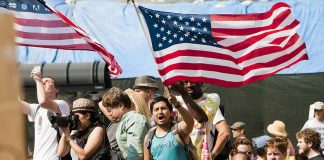 A diverse crowd at a protest holding an American flag