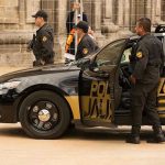 Mysterious Philadelphia Home Raid Raises More Questions Police officers standing and sitting near a patrol car.