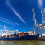 Global Tax Bombshell Hits Shipping Cargo ship docked at port with cranes unloading.
