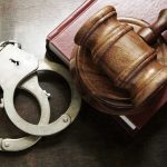 Handcuffs beside a gavel on a book.