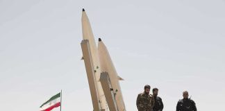 Report of Resignation Triggers Questions Over Who Runs the State Military personnel beside missiles and Iranian flag.