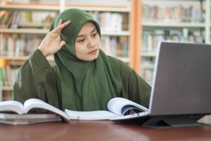 hijabi-woman-studying_2636874715 Student in green hijab studying with laptop and books in a library