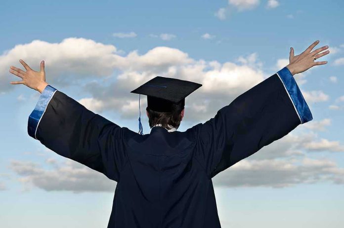 shutterstock_55937464 Graduate in cap and gown with arms raised against a blue sky