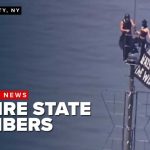 2 climbers unfurl banner at top of Empire State Building.