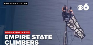 2 climbers unfurl banner at top of Empire State Building.
