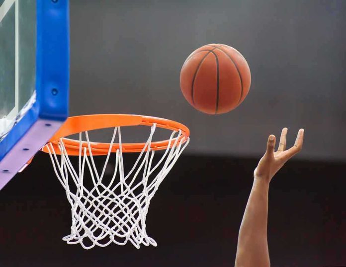 shutterstock_1448640137 Basketball nearing hoop with player’s hand reaching up