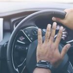 Driver's hands on a car steering wheel pressing the horn