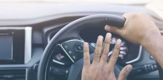 Driver's hands on a car steering wheel pressing the horn