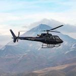 Black helicopter flying over rugged mountain range
