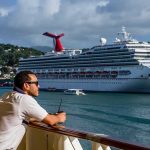 Man leaning on ship railing looking at a docked cruise ship
