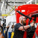 Trump Uses Michigan Auto Stop to Push His Economic Agenda Worker assembles red vehicle on factory line