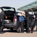 Rocket Launchers: Drugs Traded for Military Weapons customs officers detain a person beside a car with its trunk open