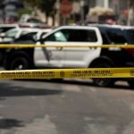 Police tape cordoning off street with patrol SUVs behind