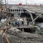 People crossing a destroyed concrete bridge over a river