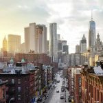 NYC Legionnaires’ Outbreak Reaches 11 Deaths City street leading to a skyline of modern and historic skyscrapers at sunset
