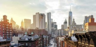 NYC Legionnaires’ Outbreak Reaches 11 Deaths City street leading to a skyline of modern and historic skyscrapers at sunset