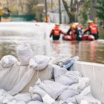 Nepal Buries Unidentified Flood Victims Sandbags stacked near a flooded street with rescue workers in a boat