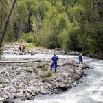 Rescue workers in helmets standing along a fast-flowing forest river
