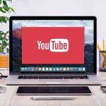 Tragic $10K Loss — AI Scammers Target Seniors! YouTube logo on a laptop screen on desk.