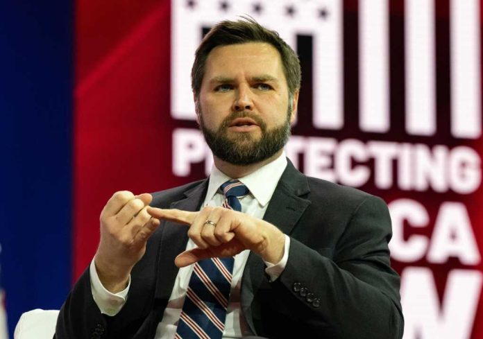 Man in suit speaking on stage with red and white backdrop
