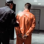 Two Brooklyn Assaults, One Arrest Police officer escorting handcuffed inmate in orange jumpsuit