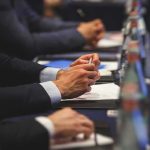 Guard Crime Claims Spark $5B Threat Hands of people in suits taking notes at a conference table