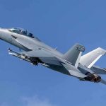 Twin-engine fighter jet climbing in a clear blue sky