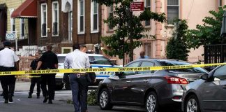 Homicide Ruling Leads to First Arrest Police at urban street crime scene with yellow tape around parked cars