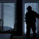 Midnight Home Invasion Targets Newborn Silhouetted person in a dark room near a door with blinds