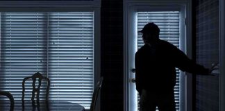 Silhouetted person in a dark room near a door with blinds