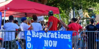 Protesters behind barricades holding a blue reparations banner