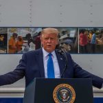 Airport Shock: Trump Meets Xi Planeside Donald Trump speaks at a podium with arms outstretched