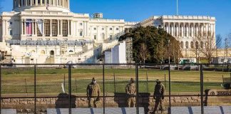 Soldiers stand behind a security fence near a large government building