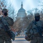 Two armed soldiers stand guard near a domed government building