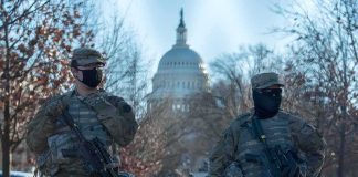 Two armed soldiers stand guard near a domed government building
