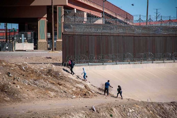 People walking along a dry canal beside a high fence with barbed wire
