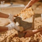 Ancient Footprints Hint At Unknown Cousin Archaeologists cleaning a large stone artifact at a dig site